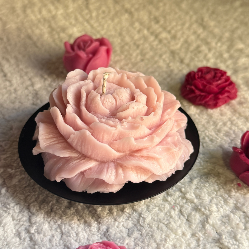 Pink flower-shaped cake on a black plate with red flowers in the background.