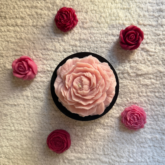 Pink rose-shaped soap in a black dish with red roses on a textured beige background